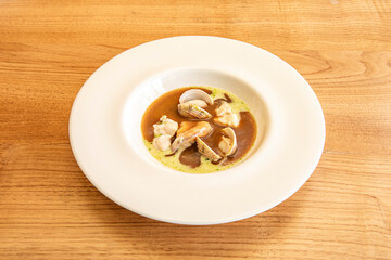 delicious fish soup with clams in white plate on wooden table