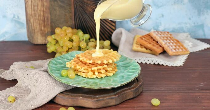 Woman pouring sweet condensed milk on tasty homemade waffles