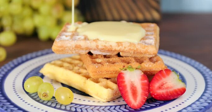 Pouring of sweet condensed milk on tasty homemade waffles
