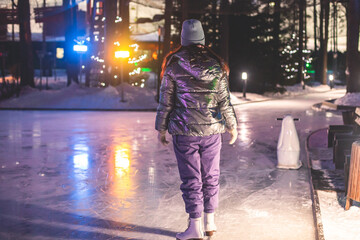 Girl ice skating on the ice rink arena with happy people in the background, concept of ice skating in winter, winter activities, holiday christmas time, with new year decoration and illumination