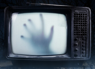 Horror photo of an old black scary haunted tv set with ghost hand on a screen, standing on dark...