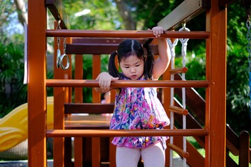 Obraz premium A cute young Asian girl is playing at a playground, trying to climb a ladder having fun and feeling happy.