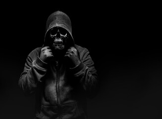 Horror photo of a scary man in hoodie with skull face on black background.