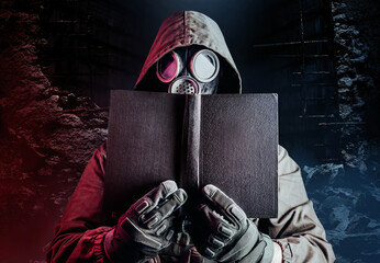 Photo of stalker soldier in soviet gas mask holding old book on destructed ruined background.