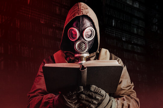 Photo of stalker soldier in soviet gas mask holding opened old book on dark background.