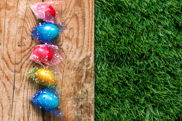 Colorful Easter eggs on the grass. Decorated easter eggs on placed on green grass against the wooden desk with copy space