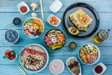 Flat-lay of various kinds of healthy food in plates and bowls on blue wood, top view.