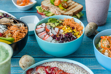 Various kinds of healthy food in plates and poke bowls on blue wood, top view.