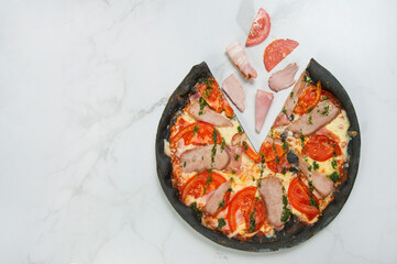 Meat black dough Pizza on white marble background with ingredients: tomato slices, ham, bacon, salami, pork and beef meat. Flying food concept. pizza served with pesto sauce. Text space
