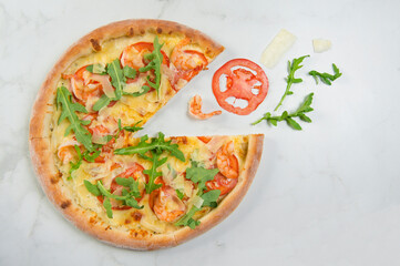 Top view of Italian seafood Pizza with green herbs on white marble background with ingredients: shrimps, Parmesan and mozzarella cheese, sliced tomatoes. Flying food concept. served with fresh arugula