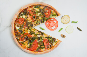 Italian veggie Pizza on white marble background with ingredients: tomato, eggplant, zucchini slices, champignon mushrooms and green beans. Flying food concept. Vegetarian pizza served with pesto sauce