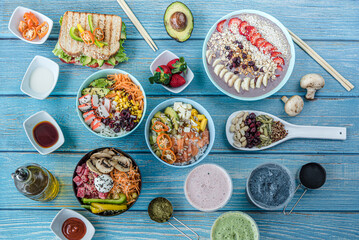 Flat-lay of various kinds of healthy food in plates and bowls on blue wood, top view.