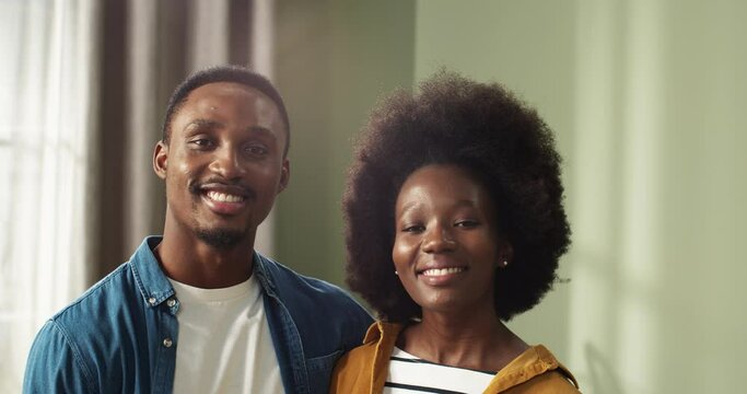 Clode up portrait of young happy african american couple in new apartment standing hugging and looking at camera smiling.