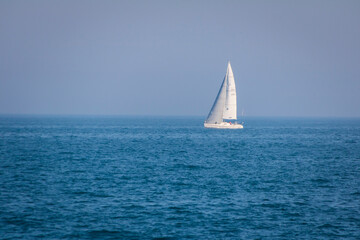 White sail boat on the horizon of blue waters.