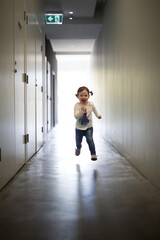 Girl toddler child running down dark corridor back lit with natural light