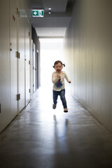 Fototapeta premium Girl caucasian toddler child running down dark corridor back lit natural light jump midair fun happy run skip