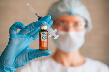 Blurred image: doctor holding syringe and coronavirus Covid-19 vaccine vial. Vaccination, pharmaceutical research concept.