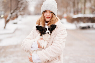 Naklejka na ściany i meble Beautiful girl with dog Papillon in her arms on winter Christmas streets
