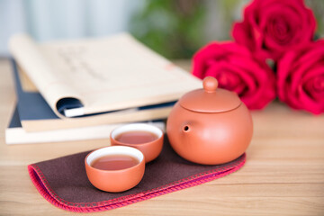 Chinese traditional tea set and traditional books with red roses next to it