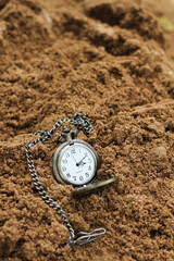 Fototapeta na wymiar a vintage pocket watch on brown sand