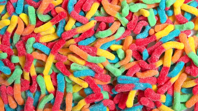 HD video above zooming on background of many sour candy gummy worms , covered in granulated sugar. 
