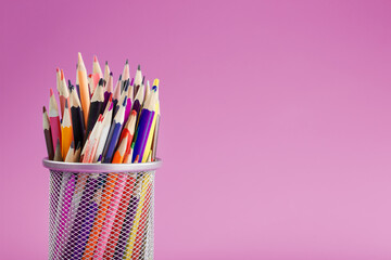 Pencils of different colors in a glass on a pink background.