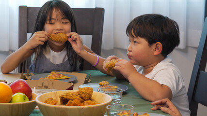 Happy Asian family relationship at home. Mother with little daughter and son eating fried chicken...