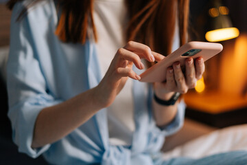 Close-up of unrecognizable young woman hands holding phone at cozy living room. Home dressed lady...