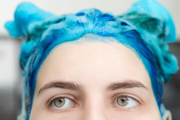 Close-up view of pretty girl with blue hair and big beautiful eyes with shampoo applied, while...