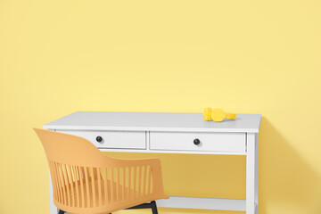 Headphones on table and chair near color wall