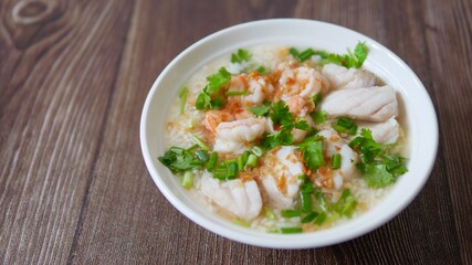 Boiled rice soup with fish and shrimp in bowl on wood background