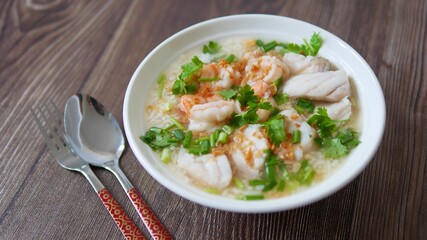 Boiled rice soup with fish and shrimp in bowl on wood background