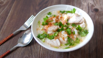 Boiled rice soup with fish and shrimp in bowl on wood background