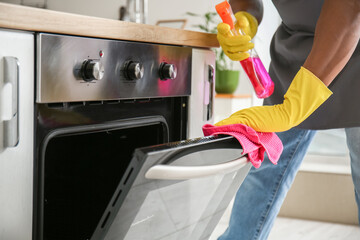 African-American man cleaning oven in kitchen