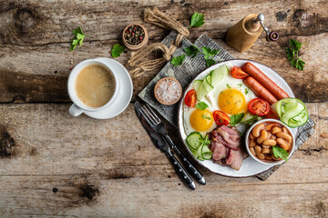 Delicious breakfast or lunch with fried eggs, beans, tomatoes, bacon on wooden background, top view