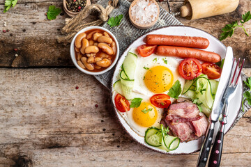 Traditional English breakfast with fried eggs, bacon, beans, coffee and sausage on wooden background, top view