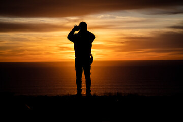 Fototapeta premium Silhouette of a man looking out at a sunset or sunrise taking a cell phone picture