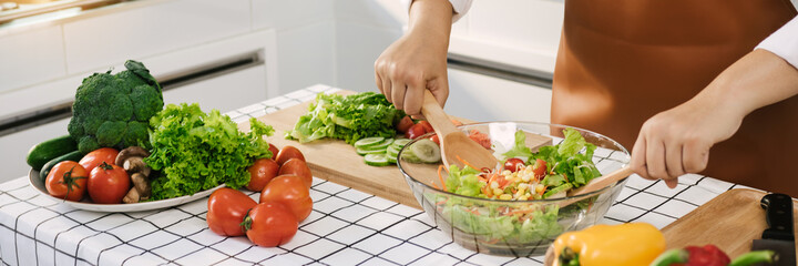 Asian woman is mixing the ingredients in a salad bowl at the kitchen cooking table.