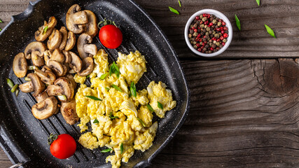 Scrambled Eggs with champignon mushrooms on frying pan for healthy breakfast or brunch, top view, copy space. Homemade meal recipe scrambled eggs