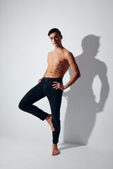 Fototapeta premium A sports guy in trousers is standing on one leg against a light background in full growth