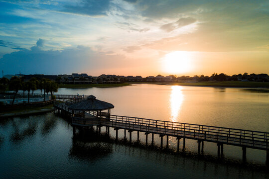 An aerial drone image of a wooden walking path over a lake during a sunset