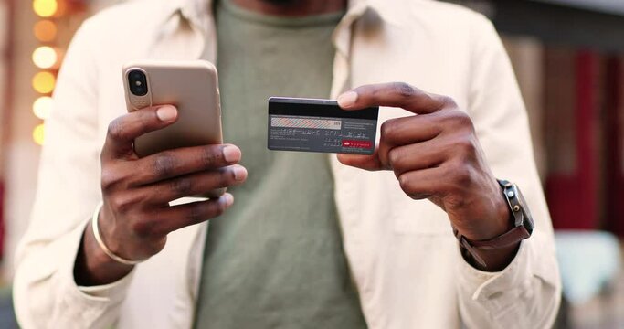 Close up of mobile phone and credit card in hands of African American young man in casual clothes. Outdoors. Shopping online concept. Buying and paying in Internet.