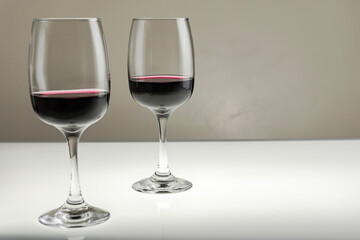 Two glasses of red wine on a blurred homogeneous background.