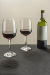 Vertical shot. Two glasses and a bottle of red wine on a blurred homogeneous background.