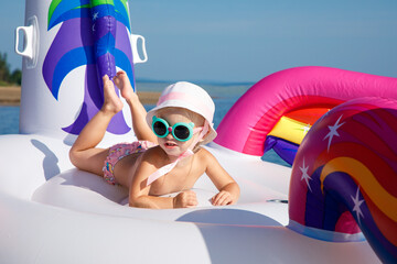 Baby girl swimming on white, trendy, blown up beach unicorn in summer in a pond, in the sea