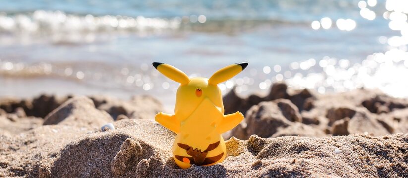 Pikachu figure model sitting on a sandy beach by the sea. Banner.	