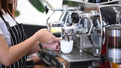 Close up view of young woman barista in apron making coffee using coffee maker at the cafe.