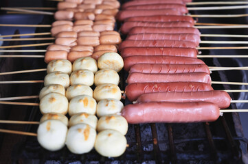 Fishball, pink big sausage and small sausage on stick are grilled on a charcoal grill.