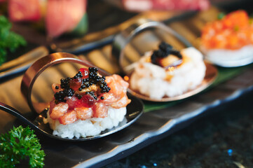 Sushi topped with Sliced salmon, foie gras, salmon egg and black tobiko on a spoon.