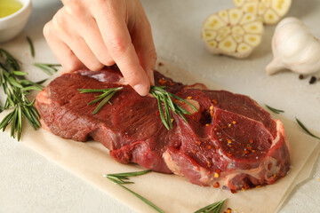 Female hand puts rosemary on raw steak meat, close up